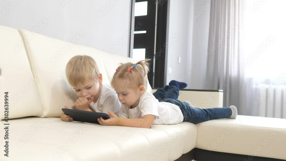 happy family concept little children play digital tablet. young kids watch videos on a white digital tablet. brother and sister are resting lying on the couch lifestyle holding tablet online chat happy family concept little children play digital tablet. young kids watch videos on a white digital tablet. brother and sister are resting lying on the couch lifestyle holding tablet online chat