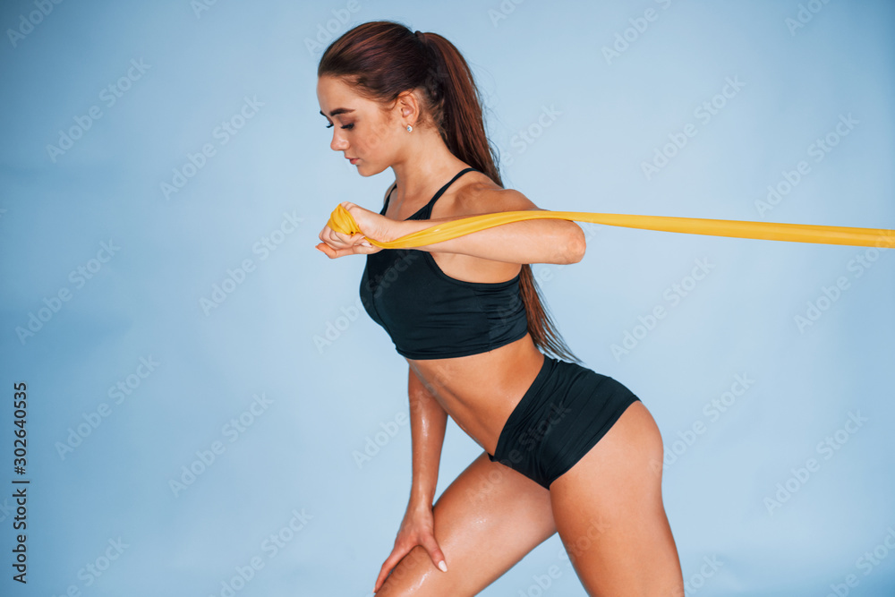 Hands exercise by using resistance band. Young woman with slim body type isolated against blue background Hands exercise by using resistance band. Young woman with slim body type isolated against blue background