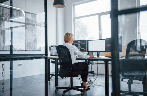 Bild auf Leinwand Female stockbroker in formal clothes works in the office with financial market