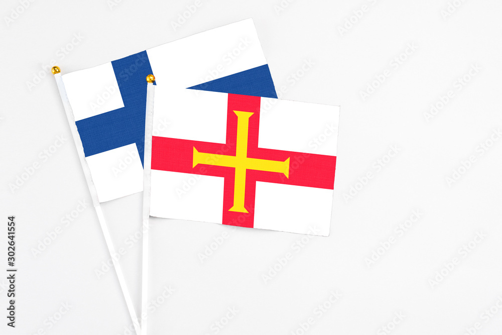Guernsey and Finland stick flags on white background. High quality fabric, miniature national flag. Peaceful global concept.White floor for copy space.