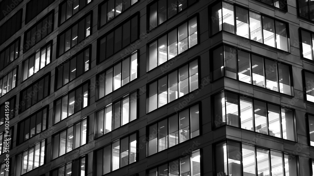 Obraz premium Pattern of office buildings windows illuminated at night. Lighting with Glass architecture facade design with reflection in urban city. Black and white.