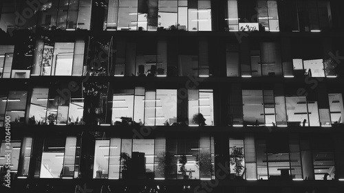 Pattern of office buildings windows illuminated at night. Lighting with Glass architecture facade design with reflection in urban city. Black and white.