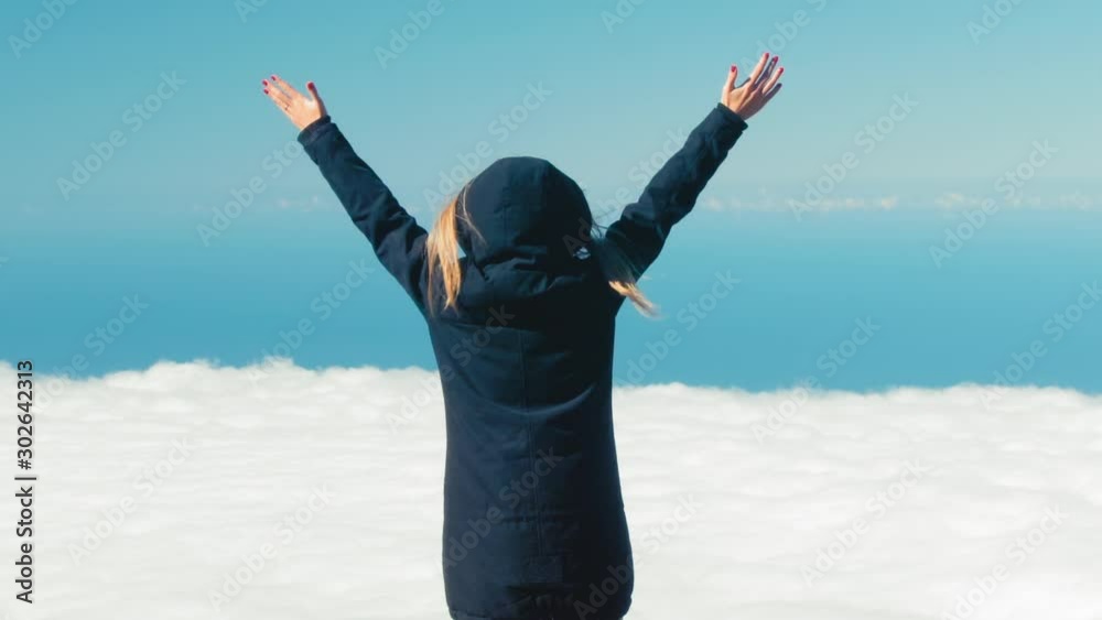 Young freedom woman standing on mountain and rise up her hand, motivation and inspiration above the clouds. Climber arms up outstretched on mountain top looking at inspirational landscape Young freedom woman standing on mountain and rise up her hand, motivation and inspiration above the clouds. Climber arms up outstretched on mountain top looking at inspirational landscape
