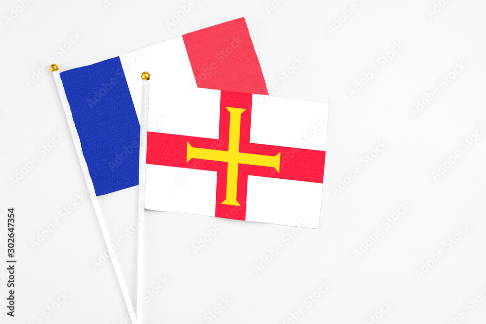 Guernsey and France stick flags on white background. High quality fabric, miniature national flag. Peaceful global concept.White floor for copy space.