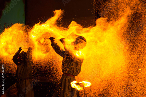 Fire show: two people in protective suits twist coal props over their heads, spreading sparks around themselves