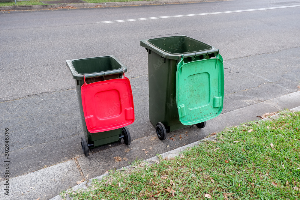 Australian garbage wheelie bins with colourful lids for recycling household waste and green garden waste lined up on the street kerbside for council rubbish collection Australian garbage wheelie bins with colourful lids for recycling household waste and green garden waste lined up on the street kerbside for council rubbish collection