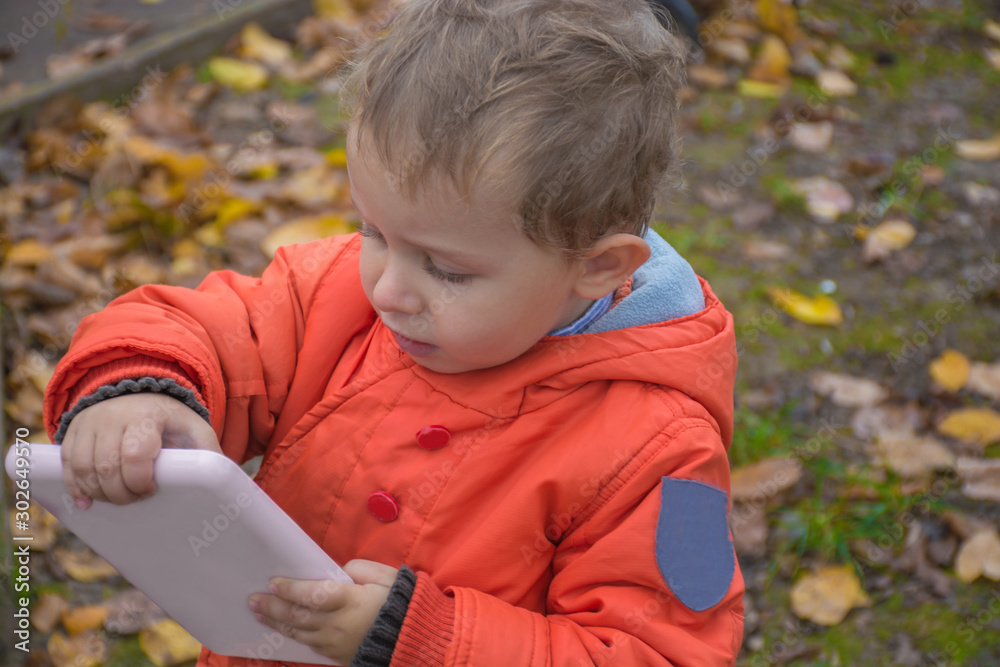 Little caucasian boy, 3 years old, in orange jacket and jeans is going to school. Child used laptop on park. Kid play game on laptop. Preschool education knowledge concept.