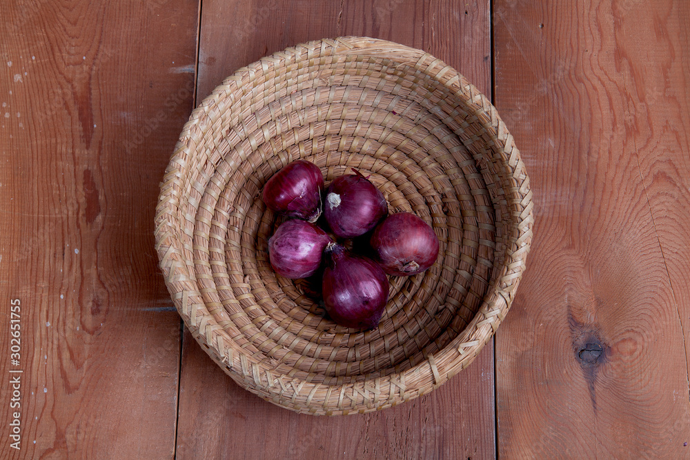  Onion in wicker basket on the wooden table.