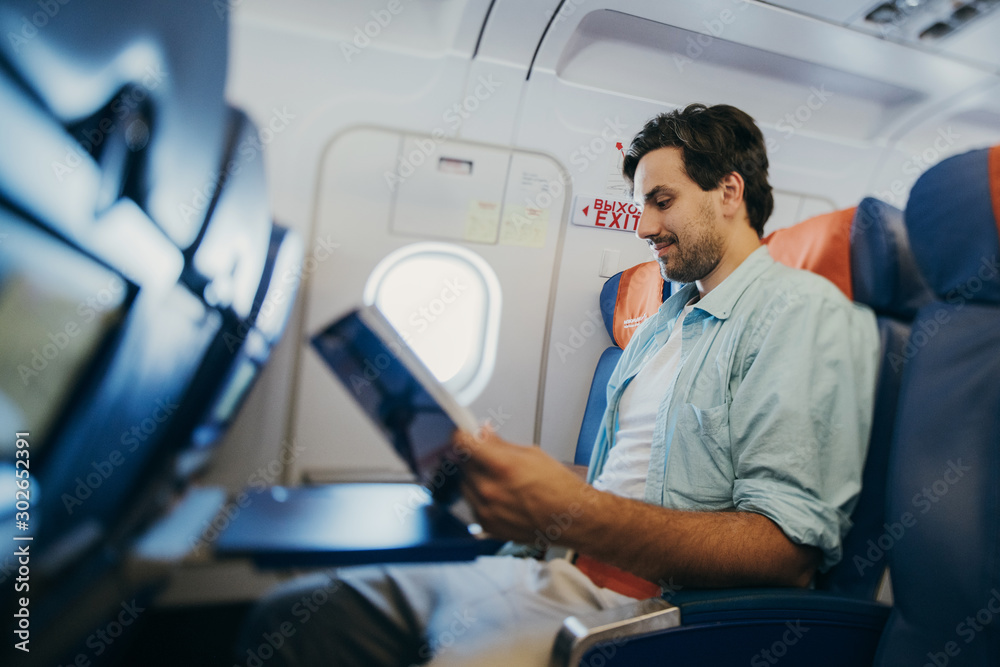Fototapeta premium The guy flies in an airplane with a magazine in his hands