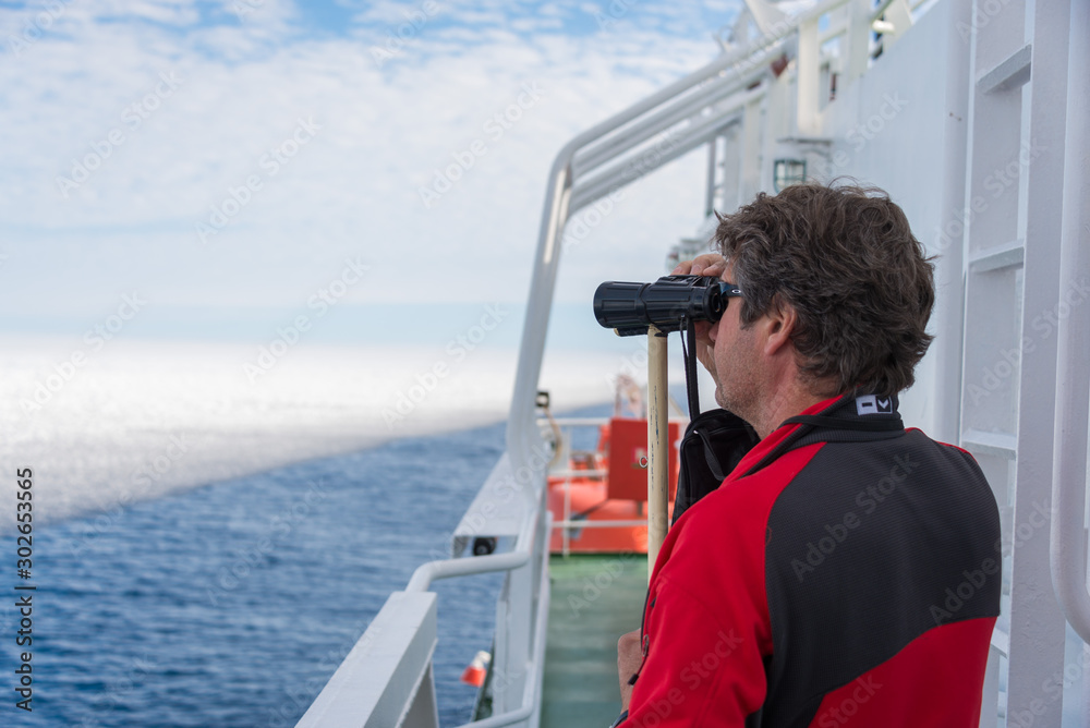 Man with binoculars on the navigational bridge looking Man with binoculars on the navigational bridge looking