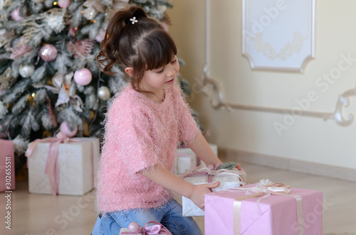 Beautiful little girl on christmas tree background. Cute little girl in pink holding gift. Christmas. New Year. Holiday. Indoor. Home.