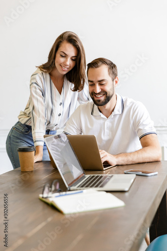 Smiling colleagues work with laptop talking with each other.