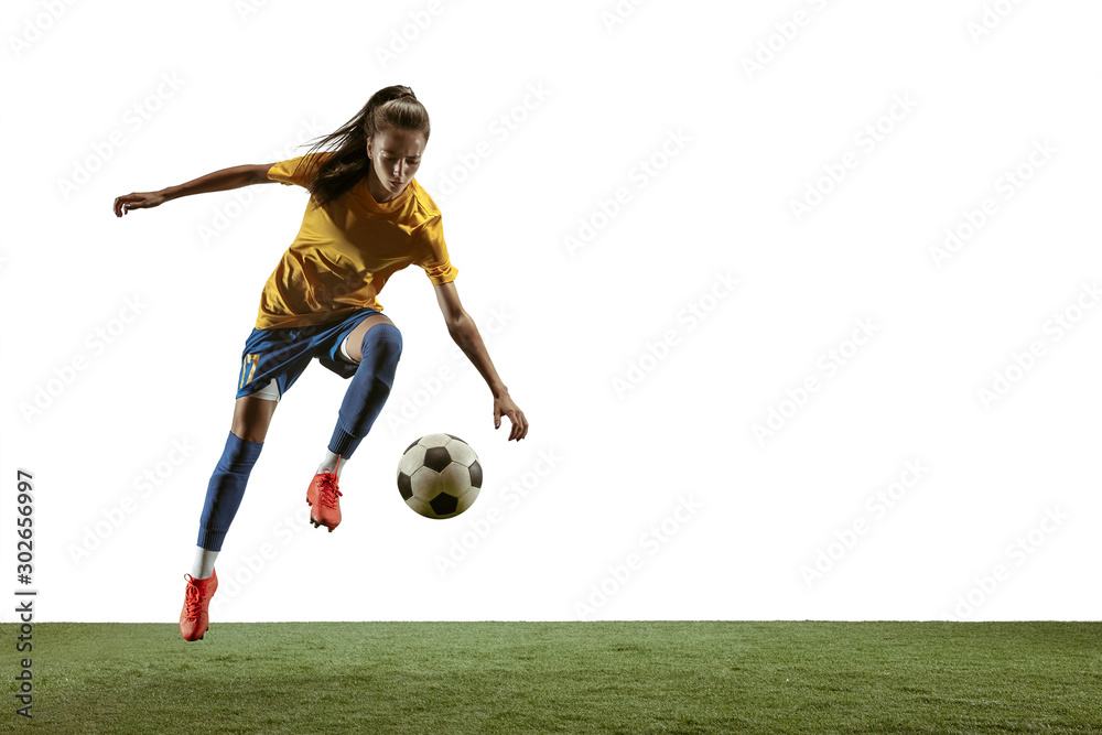 Young female soccer or football player with long hair in sportwear and boots kicking ball for the goal in jump on white background. Concept of healthy lifestyle, professional sport, motion, movement.