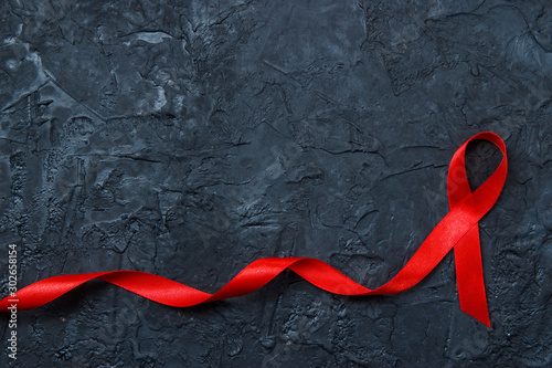 Red ribbon as symbol of aids awareness on black background. Medical care campaign