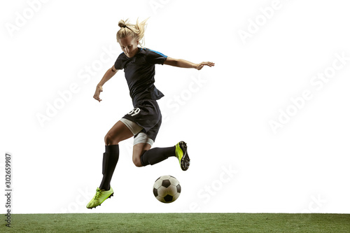 Young female soccer or football player with long hair in sportwear and boots kicking ball for the goal in jump on white background. Concept of healthy lifestyle, professional sport, motion, movement.