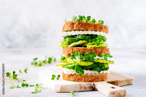 Avocado, cucumber and feta cheese sandwich decorated with micro-greens and multi-grain bread on a simple wooden stand for a healthy breakfast. Selective focus.
