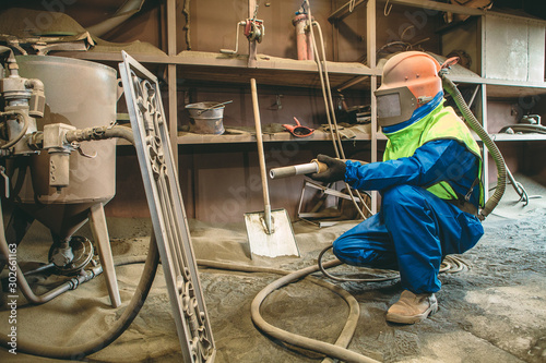 An employee prepares a metal part for painting. A harsh man works in the factory. Sandblast. Blast it. photo