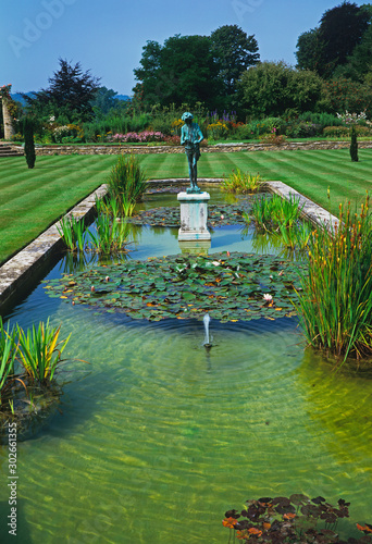 A decorative garden pool with water lilies and a classicl statue in the centre of a large lawn photo