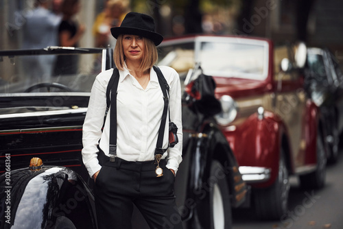 Blonde woman in hat and in black retro clothes near old vintage classic car © standret