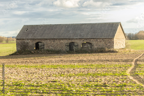 Autumn sunset. An abandoned stone barn stands in the middle of a plowed field. Side facade. Industrial dairy farm. Podlasie, Poland.