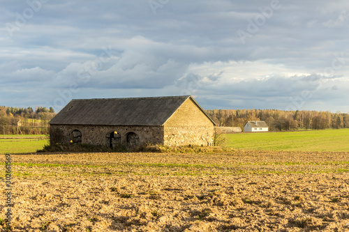 An abandoned stone barn stands in the middle of a plowed field. Industrial dairy farm. Podlasie, Poland.