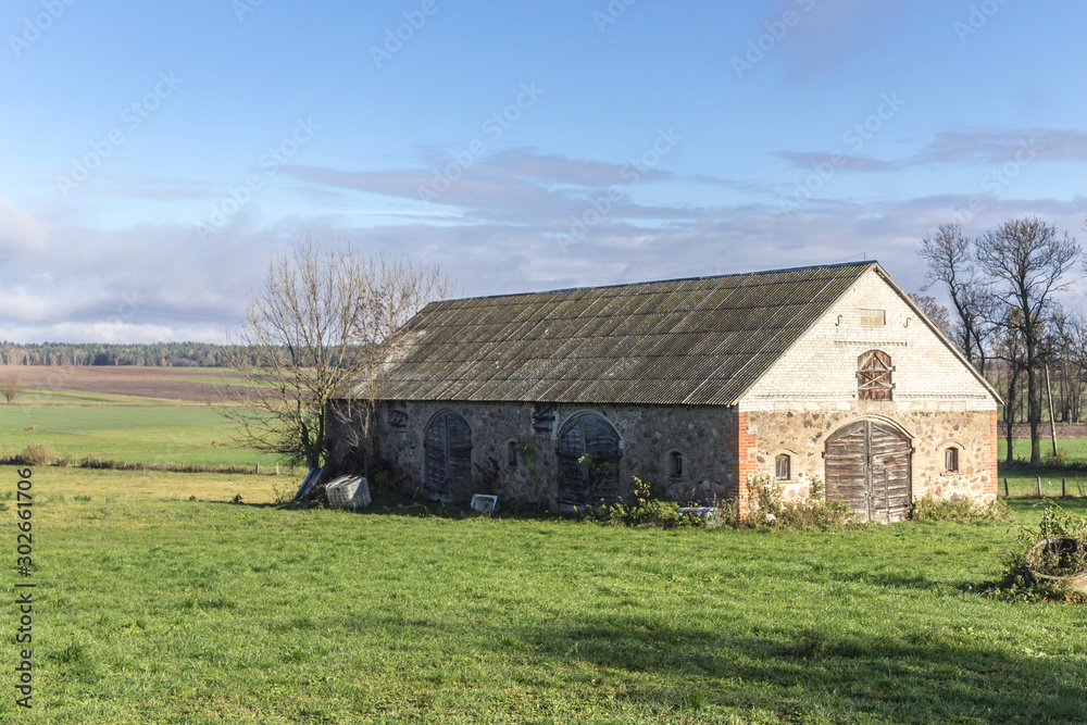An abandoned stone barn stands in a green meadow. Industrial dairy farm. Podlasie, Poland. An abandoned stone barn stands in a green meadow. Industrial dairy farm. Podlasie, Poland.