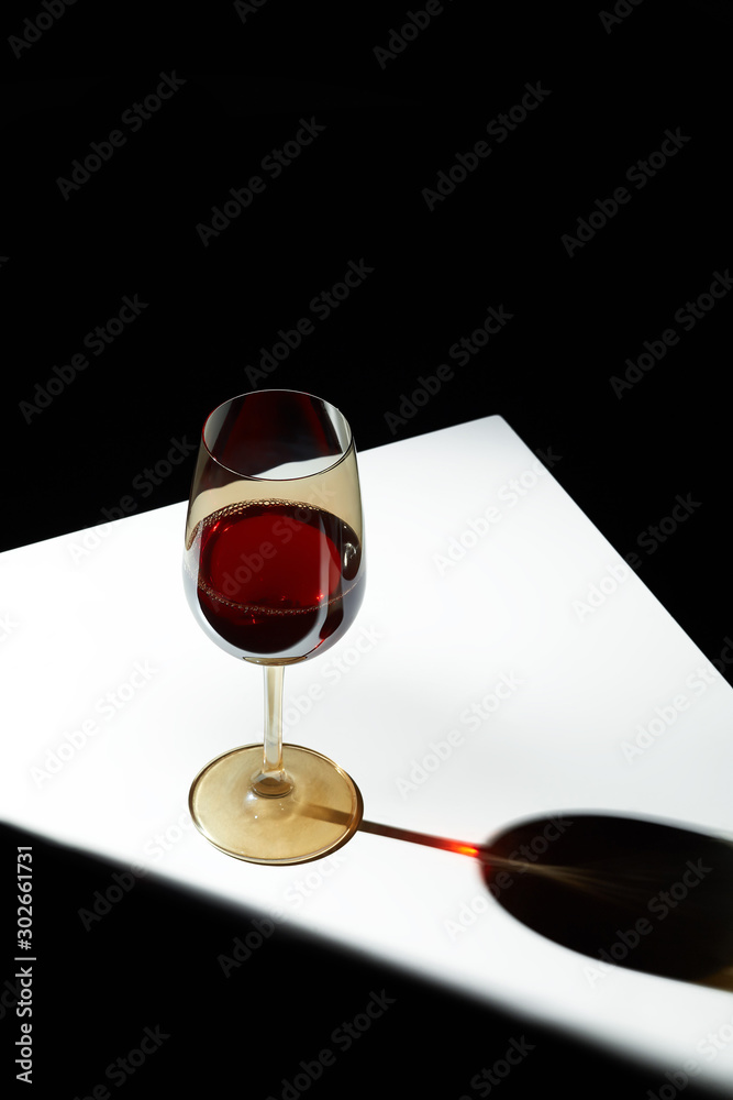 Object shot of a golden wineglass, staying on a white table. The light falls on the glass, the glass casts a shadow. The glass is half full of wine. Object shot of a golden wineglass, staying on a white table. The light falls on the glass, the glass casts a shadow. The glass is half full of wine.