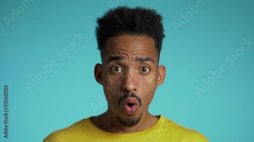 Amazed mixed race man shocked, saying WOW. Handsome african american guy with afro hair surprised to camera over blue background. photo