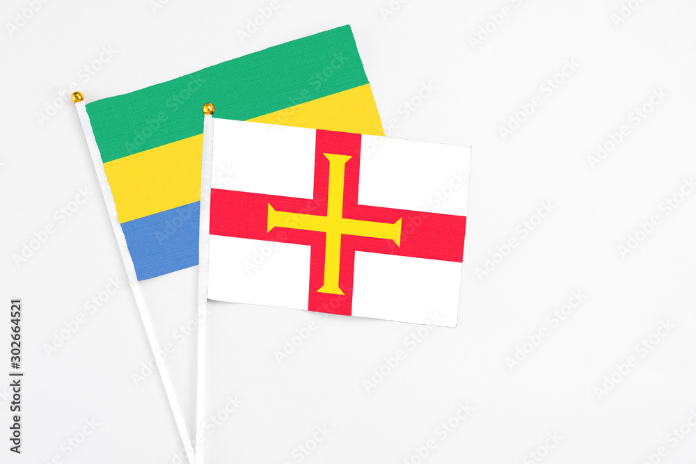 Guernsey and Gabon stick flags on white background. High quality fabric, miniature national flag. Peaceful global concept.White floor for copy space.