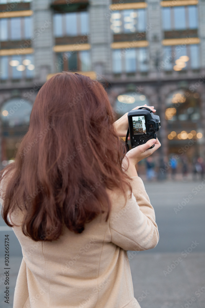 Unrecognizable person standing with his back turned and photographs sights, woman with long thick dark hair, tourist in center of St. Petersburg. Focus on camera