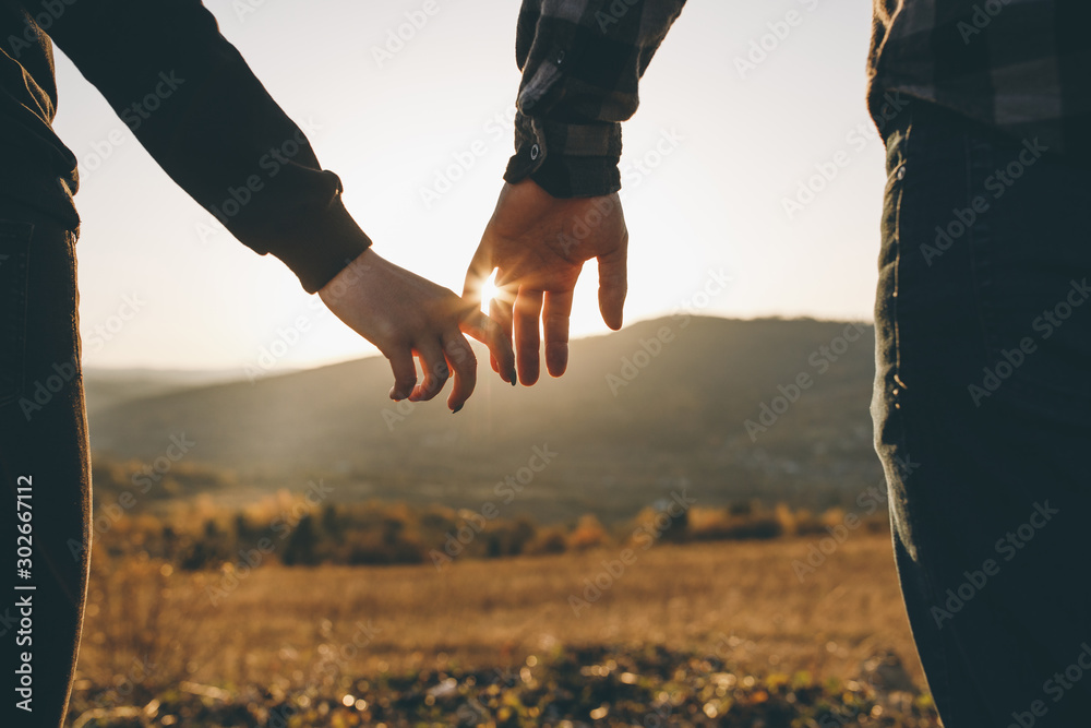 Close-up of hands joining together with sunlight flare in the background. Beautiful romantic moment between two lovers - obrazy, fototapety, plakaty 