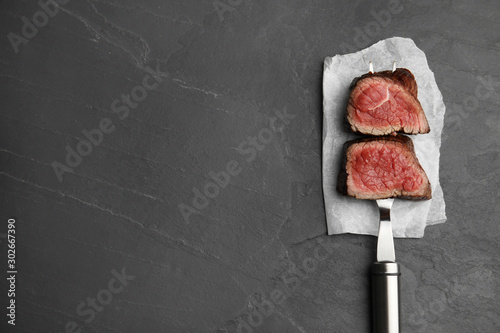 Carving fork with slices of delicious beef tenderloin on black table, top view. Space for text