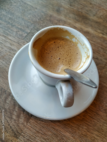 Espresso with latte in a white cup and plate served on wooden table on a break with fresh and warm beverage