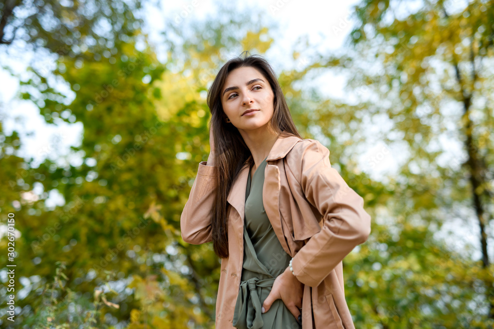 Portrait of brunette woman in green dress posing in autumn park