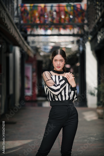 street portrait, strong woman in black, confident woman, lady in city, portrait of Asian female, half body ,posing her hands on one shoulder wearing stripe top