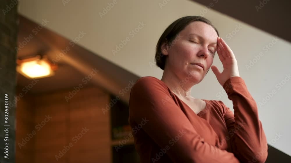 Woman with migraine headache standing by the kitchen loft window Woman with migraine headache standing by the kitchen loft window
