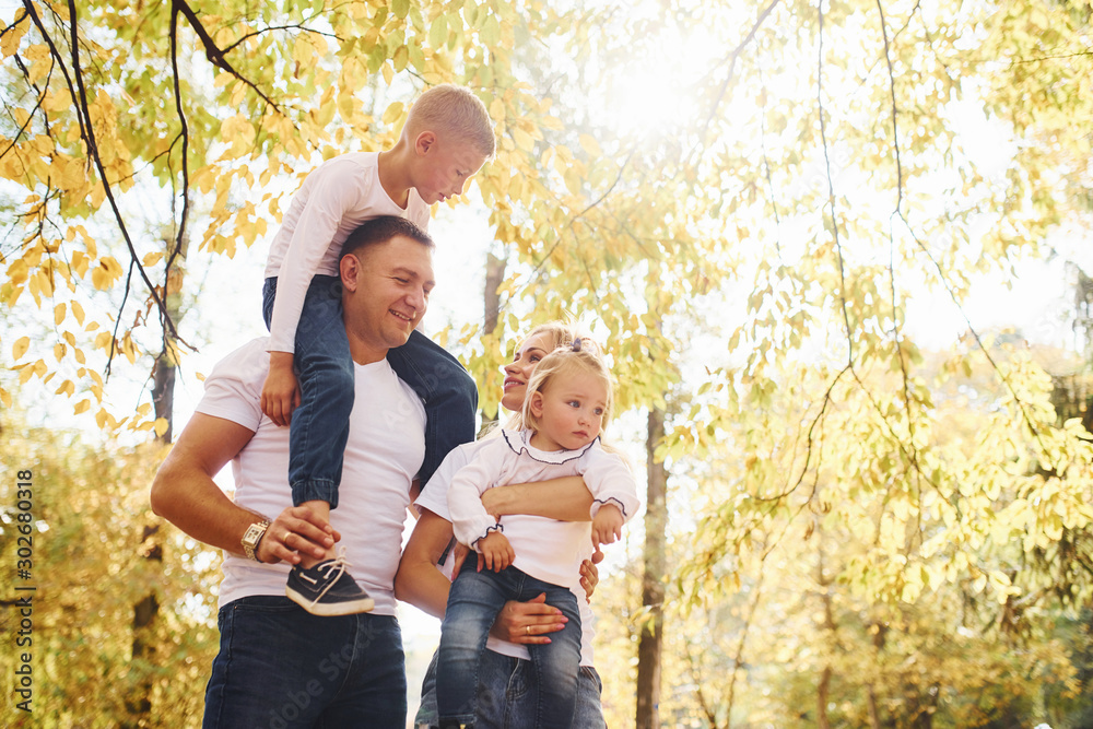 Mother and dad holds kids at shoulders and in hands. Cheerful young family have a walk in an autumn park together Mother and dad holds kids at shoulders and in hands. Cheerful young family have a walk in an autumn park together