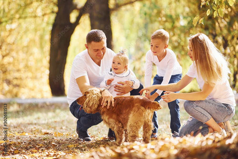 Cheerful young family with dog have a rest in an autumn park together