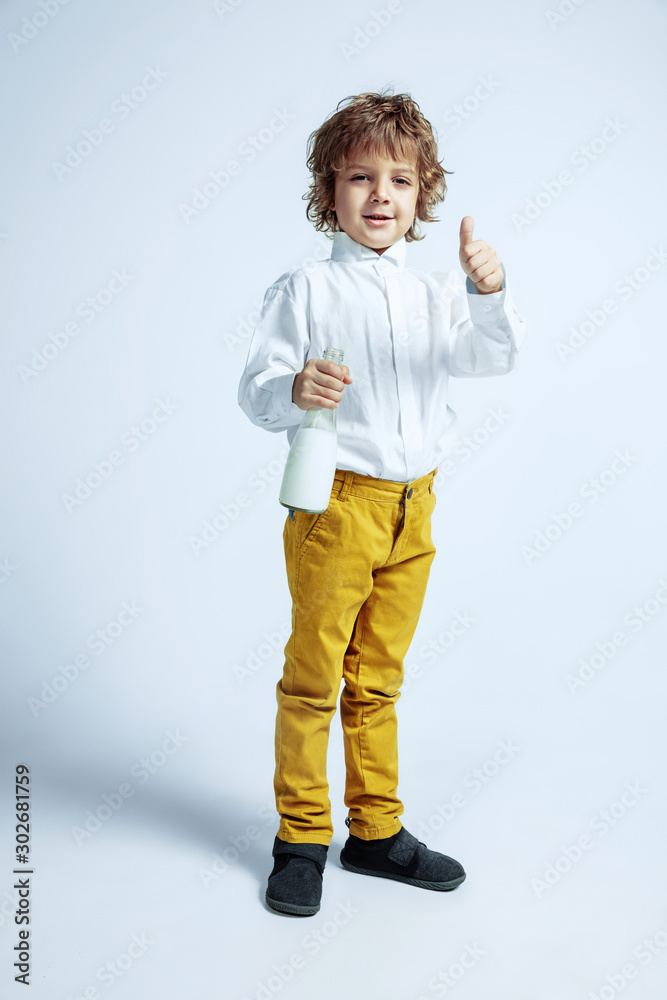 Pretty young boy in casual clothes on white studio background. Fashionable posing. Caucasian male preschooler with bright facial emotions. Childhood, expression, having fun. Drinking milk, thumb up. Pretty young boy in casual clothes on white studio background. Fashionable posing. Caucasian male preschooler with bright facial emotions. Childhood, expression, having fun. Drinking milk, thumb up.