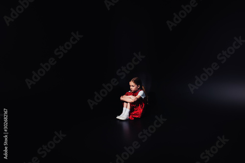 depressed, frightened kid sitting on floor isolated on black