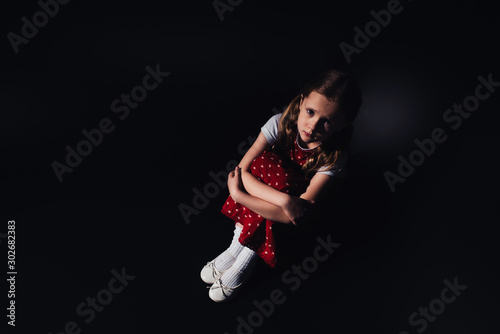 sad, scared child sitting on floor and looking at camera on black background