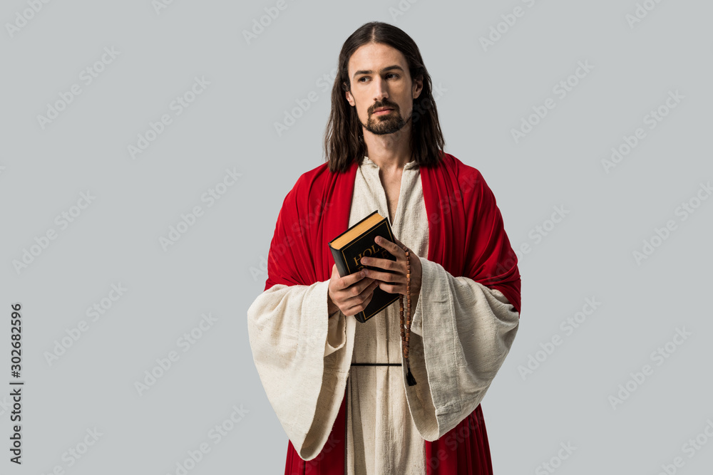 handsome man looking at camera while holding holy bible isolated on grey