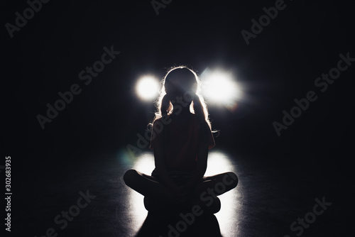 child sitting in darkness illuminated by headlights on black background photo
