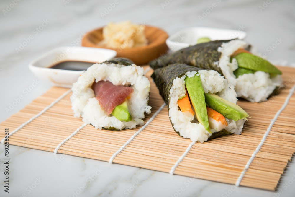 Lachs Fisch, Tunfisch und Surimi Avocado Temaki Sushi, eingelegter Ingwer mit Soja Soße und Sushimatte auf Marmor Hintergrund Lachs Fisch, Tunfisch und Surimi Avocado Temaki Sushi, eingelegter Ingwer mit Soja Soße und Sushimatte auf Marmor Hintergrund