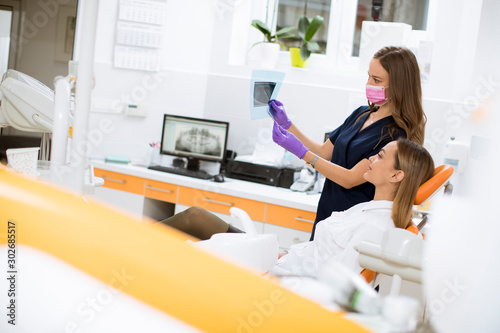 Young female doctor with protective gloves examining radiograph with her patient in the dentist office