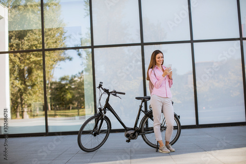 Young woman using mobile phone by modern city electric e-bike as clean sustainable urban transportation