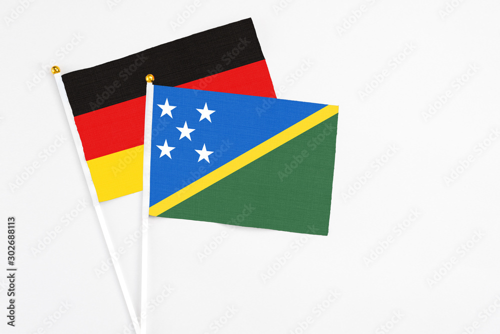Fototapeta premium Solomon Islands and Germany stick flags on white background. High quality fabric, miniature national flag. Peaceful global concept.White floor for copy space.