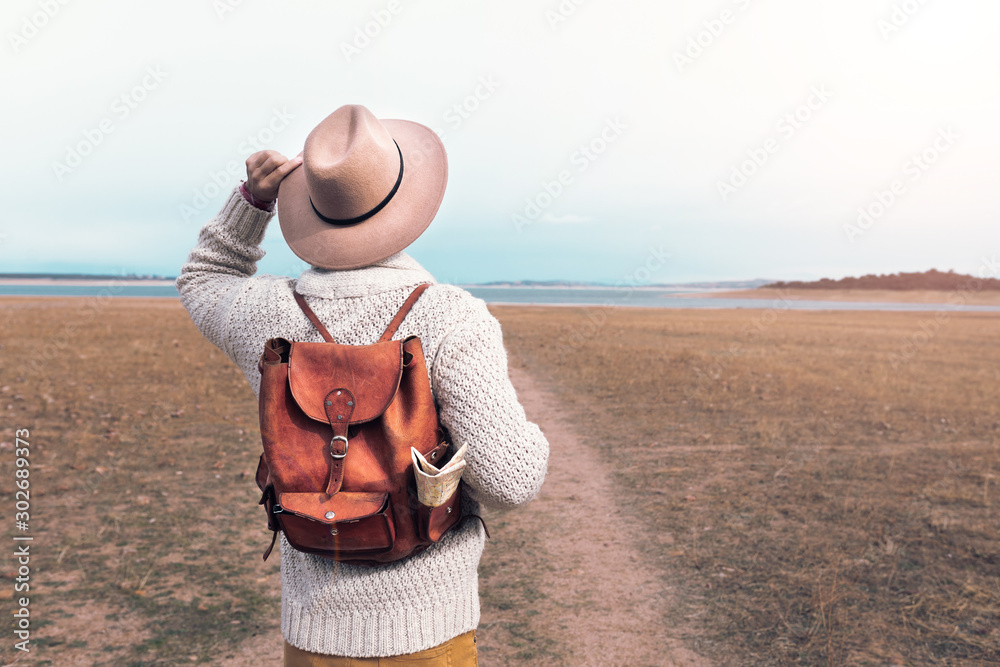 young man traveling through nature with backpack and hat - obrazy, fototapety, plakaty 
