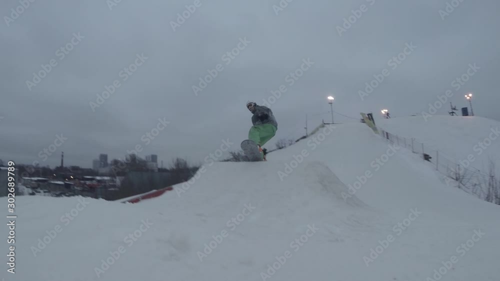 A snowboarder in bright sportswear doing the trick on the springboard A snowboarder in bright sportswear doing the trick on the springboard