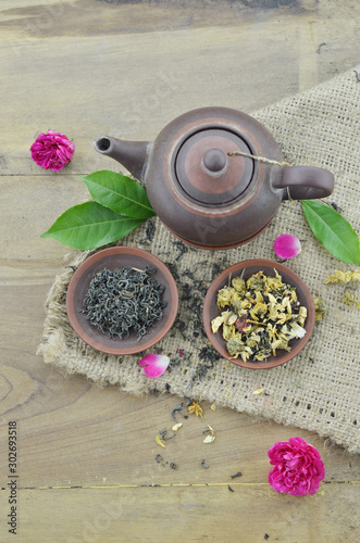 Dry tea in plate and teapot on wooden background